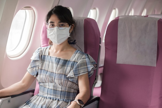 Young woman wearing protective face mask in airplane or public transportation, protection coronavirus disease infection, asian tourist ready to travel. next normal and reopening concept