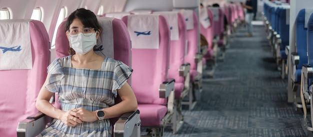Молодая женщина в защитной маске в самолете или общественном транспорте, защита от коронавирусной инфекции, азиатский турист готов к путешествию. next normal и концепция открытия