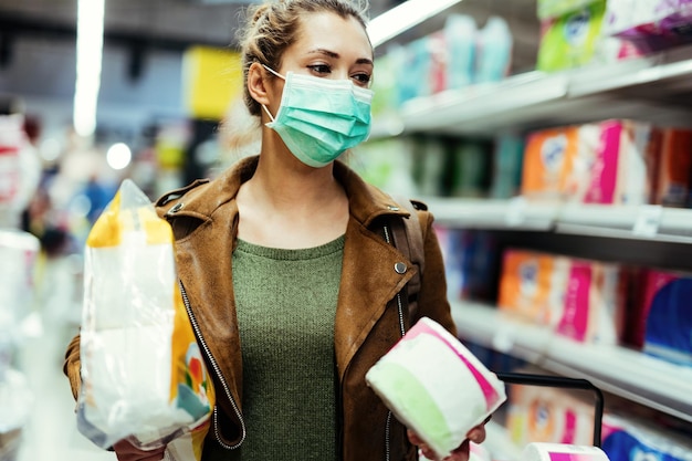 바이러스 전염병 동안 가게에서 화장지를 쇼핑하는 동안 보호 마스크를 쓴 젊은 여성