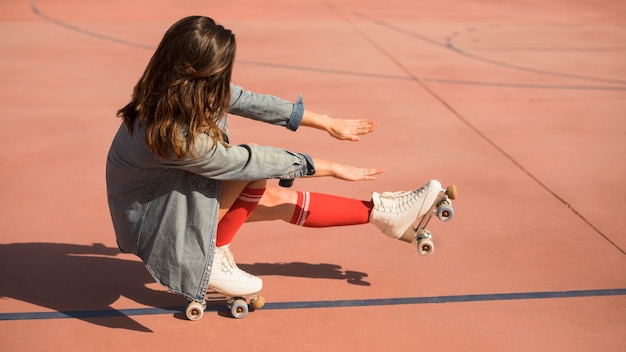 Young woman wearing roller skates crouching and stretching her legs and hand on court