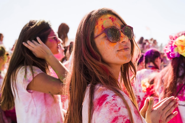 Young woman wearing sunglasses and playing with holi color, looking at the camera