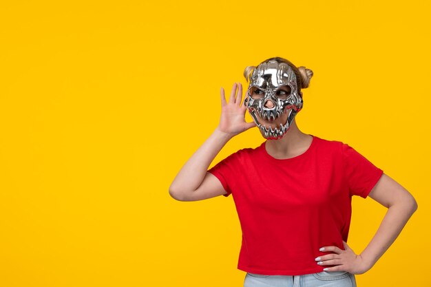 Young woman wearing terrifying golden mask yellow background horror