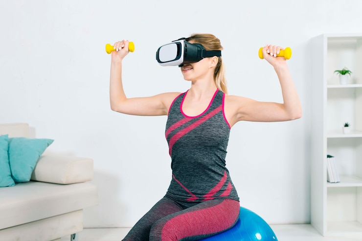 Free Photo young woman wearing the virtual reality headset sitting on the fitness ball exercising with yellow dumbbells