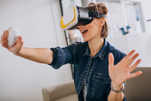 Young woman wearing VR glasses and playing virtual game using remote