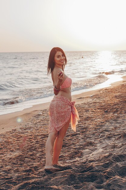 熱帯のビーチで海の景色を眺めながらポーズをとって白いビキニを着ている若い女性