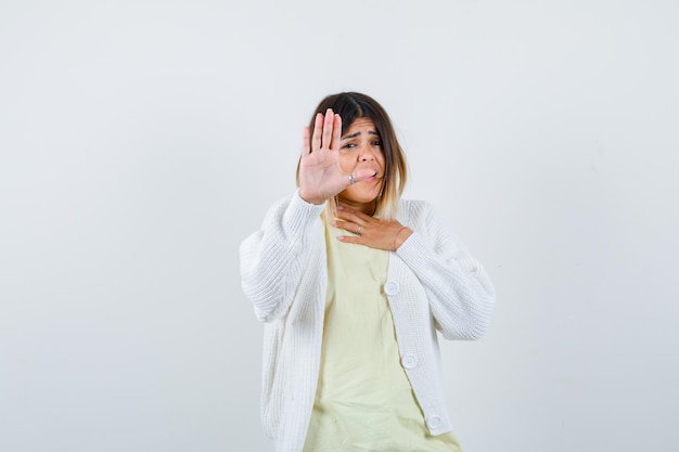 Young woman wearing a white cardigan showing stop gesture