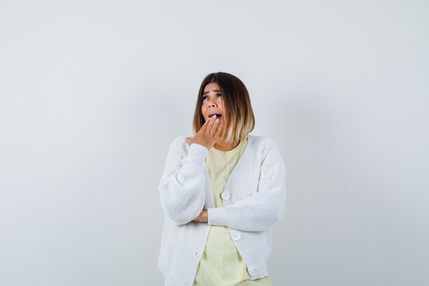 Young woman wearing a white cardigan yawning