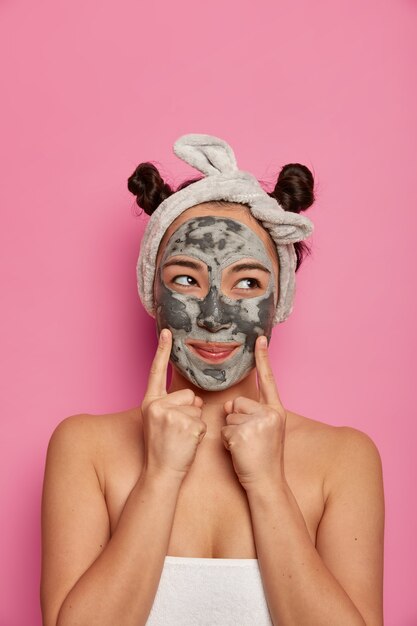 Молодая женщина носит маски для лица из натуральной глины для ухода за кожей после принятия ванны