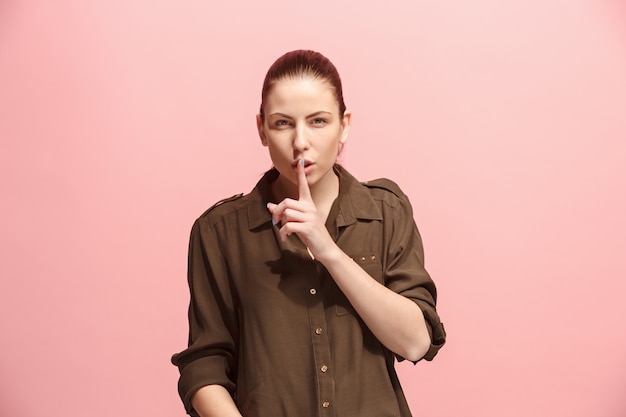 The young woman whispering a secret behind her hand over pink wall