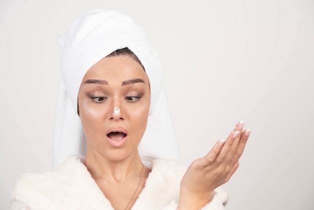 Free photo young woman in a white bathrobe applying a cream on her nose