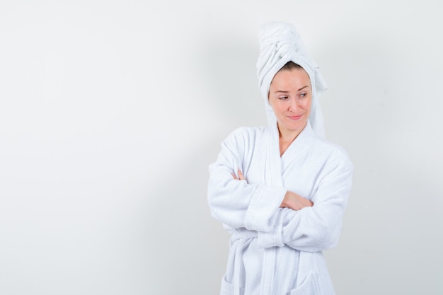 Young woman in white bathrobe, towel standing with crossed arms and looking pensive , front view.