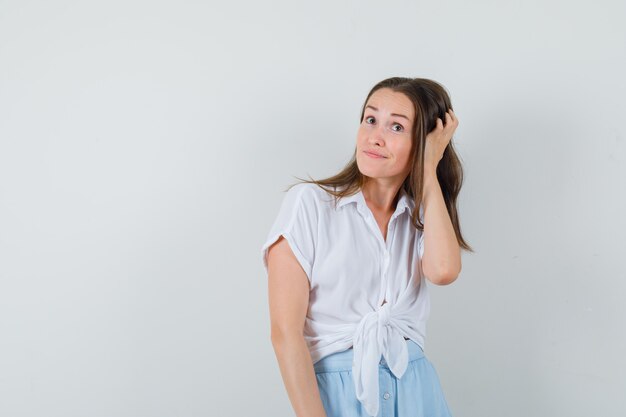 Young woman in white blouse and light blue skirt scratching head and looking cheerful