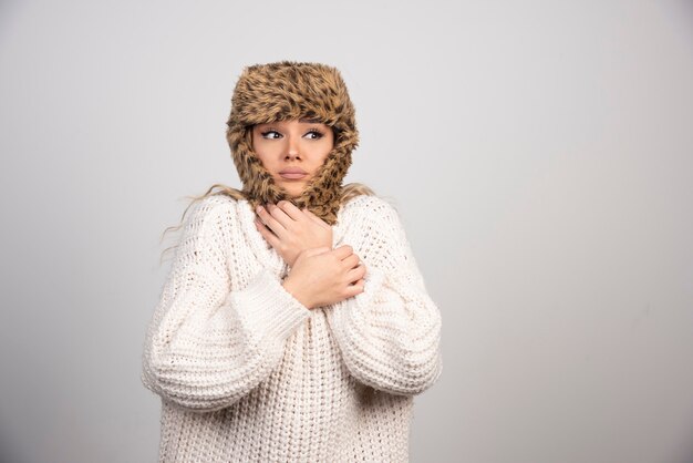 Young woman in white knitted sweater feeling cold. 