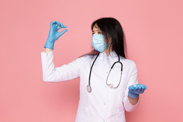 молодая женщина в белом медицинском костюме синие перчатки синие защитные маски, держа таблетки на розовый