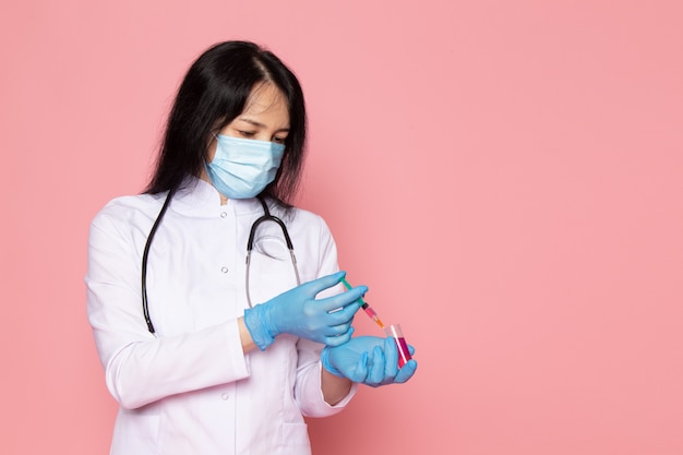 молодая женщина в белом медицинском костюме синие перчатки голубая защитная маска на розовом