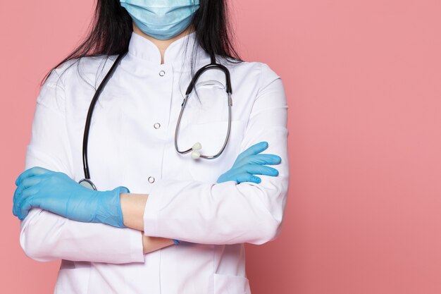 young woman in white medical suit blue gloves blue protective mask with stethoscope on pink