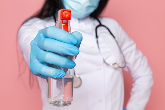 молодая женщина в белом медицинском костюме синие перчатки голубая защитная маска со стетоскопом на розовом