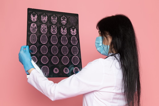 young woman in white medical suit blue gloves blue protective mask with stethoscope on pink