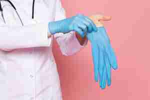 Free photo young woman in white medical suit blue gloves blue protective mask with stethoscope on pink