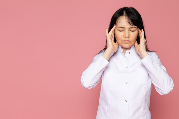 young woman in white medical suit having a severe headache on pink