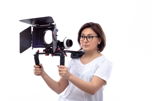 Young woman in white shirt and black glasses holding television camera