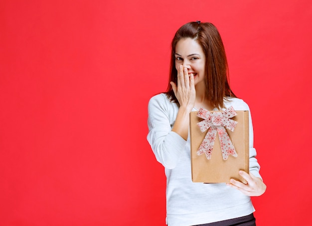 Young woman in white shirt holding a cardboard gift box, covering mouth and smiling