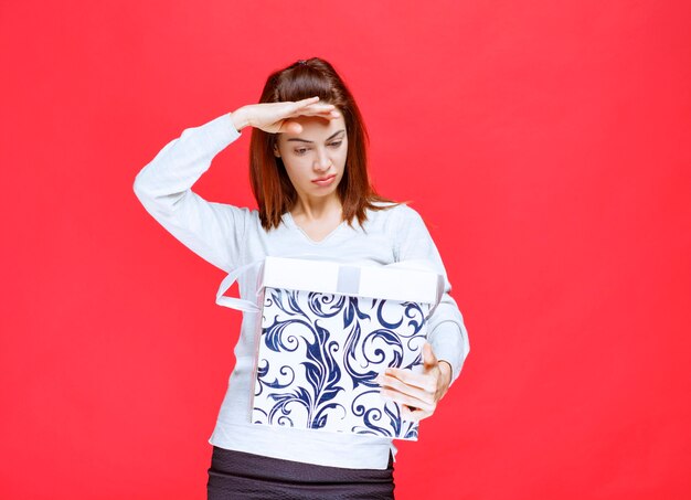 Young woman in white shirt holding a printed gift box and looks dissatisfied and upset