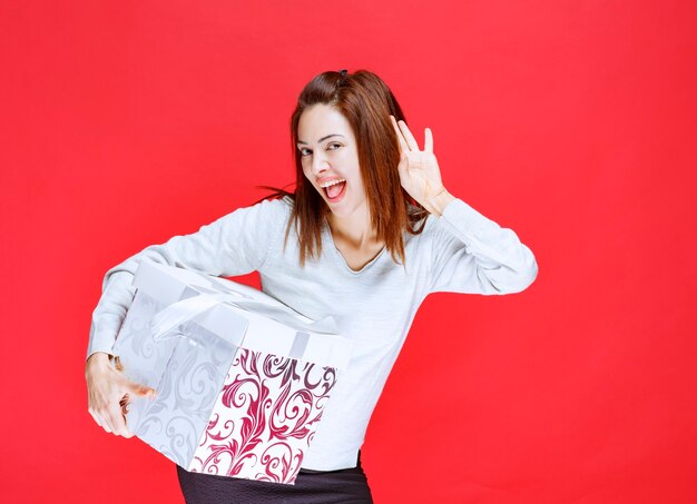 Young woman in white shirt holding a printed gift box, screaming and putting tongue out