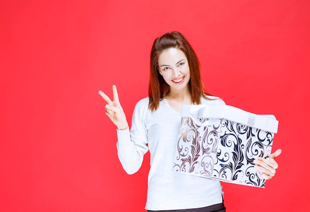 Young woman in white shirt holding a printed gift box and showing positive hand sign