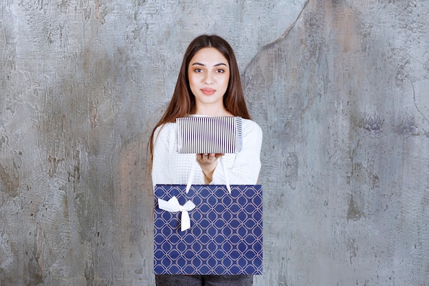 Young woman in white shirt holding a silver gift box and a blue shopping bag