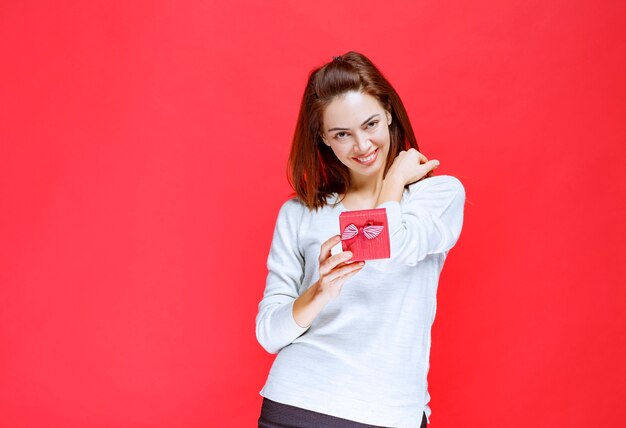 Молодая женщина в белой рубашке держит небольшую красную подарочную коробку
