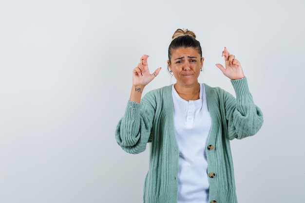 Foto gratuita giovane donna in camicia bianca e cardigan verde menta che tiene le dita incrociate e sembra tormentata