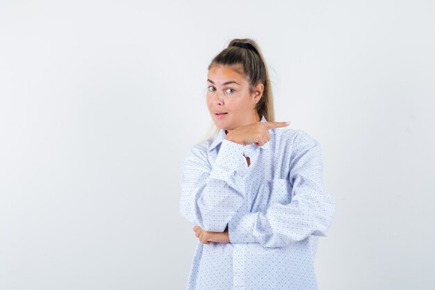 Young woman in white shirt pointing right with index finger and looking cute