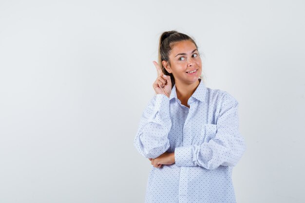 Young woman in white shirt raising index finger in eureka gesture and looking sensible