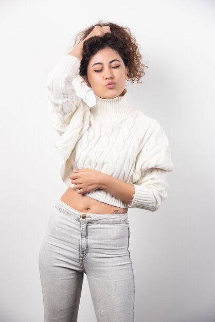 Young woman in white sweater doing funny face over a white wall. High quality photo