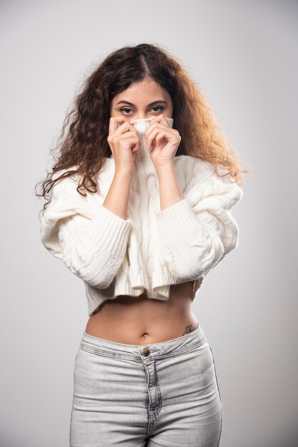 흰 벽 위에 서있는 흰색 스웨터에 젊은 여자. 고품질 사진