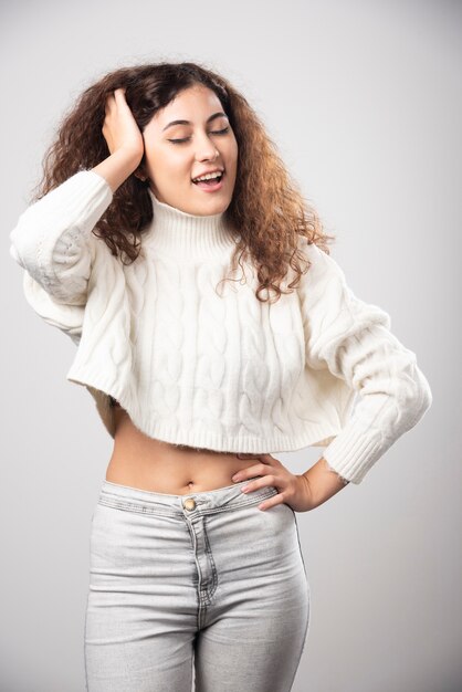 Young woman in white sweater standing over a white wall. High quality photo