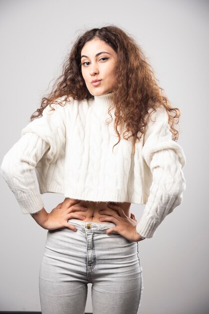 Young woman in white sweater standing over a white wall. High quality photo