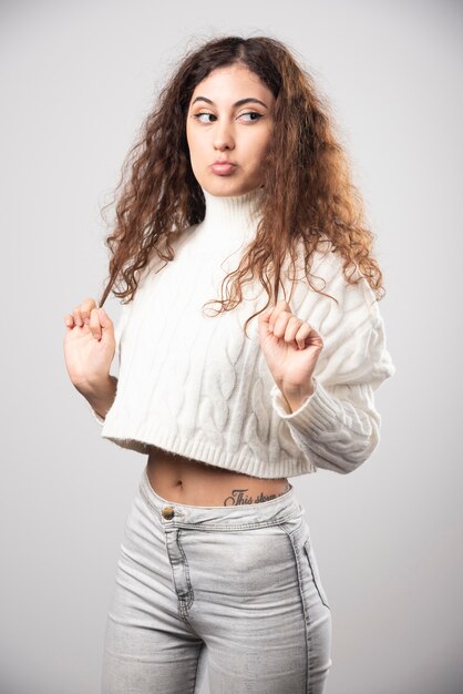 Young woman in white sweater standing over a white wall. High quality photo