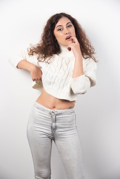 Young woman in white sweater standing over a white wall. High quality photo