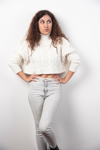 Young woman in white sweater standing over a white wall. High quality photo