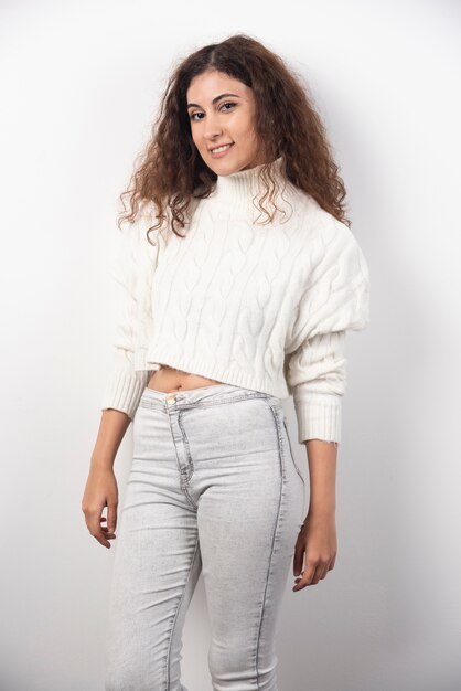 Young woman in white sweater standing over a white wall. High quality photo