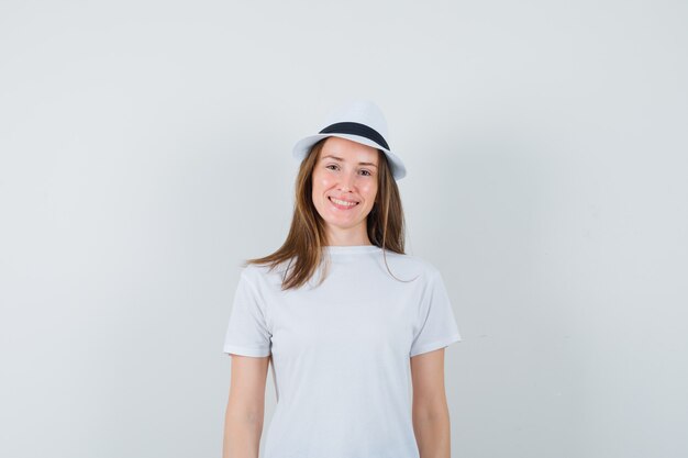 Молодая женщина в белой футболке, шляпе и выглядит веселой.