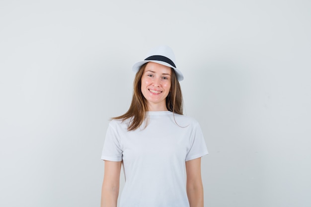 Молодая женщина в белой футболке, шляпе и выглядит веселой.