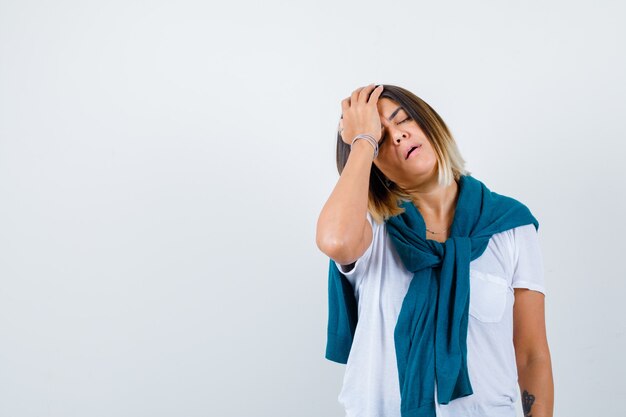 Young woman in white t-shirt holding head with hand and looking painful , front view.