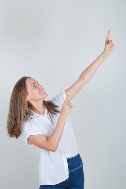 Free photo young woman in white t-shirt, jeans pointing away fingers and looking cheerful