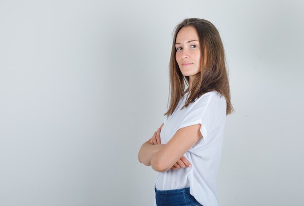 Young woman in white t-shirt, jeans standing with crossed arms and looking cheerful .