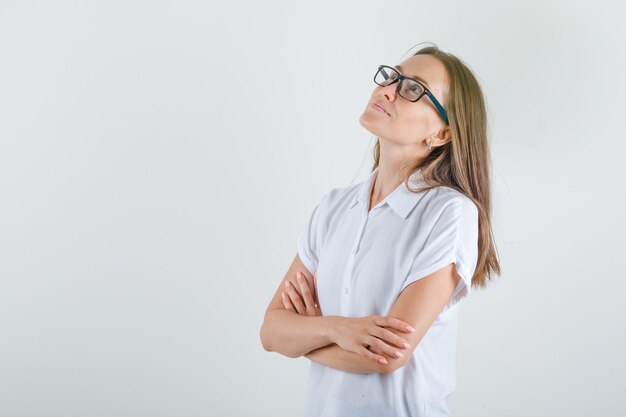 腕を組んで見上げて希望に満ちた白いTシャツの若い女性。