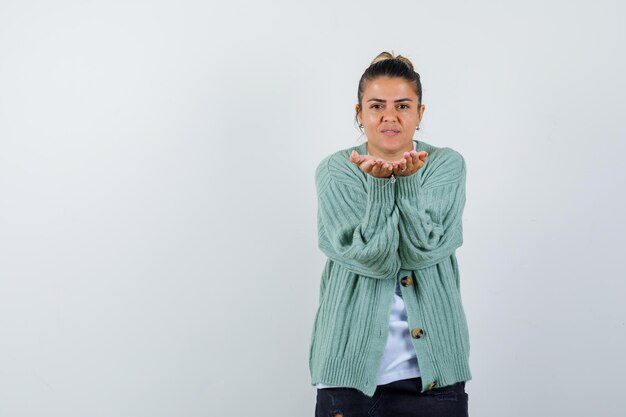 Young woman in white t-shirt and mint green cardigan inviting to come and looking serious