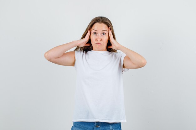 Young woman in white t-shirt, shorts holding hands on head and looking confused